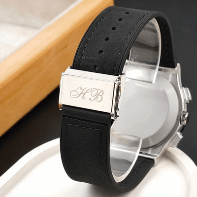 Men's wristwatch close-up: black leather strap buckle with engraved initials on silver case